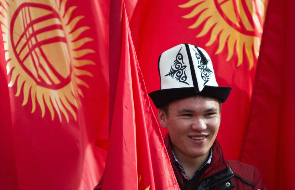 A man wearing a Kyrgyz national hat poses with national flags before a rally marking the Day of Flag and the Day of Kolpak in Bishkek, Kyrgyzstan on 4th March, 2013
