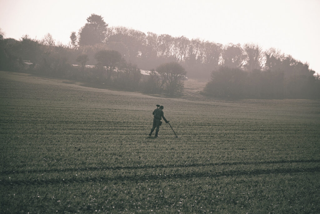 An individual uses a metal detector in a field.