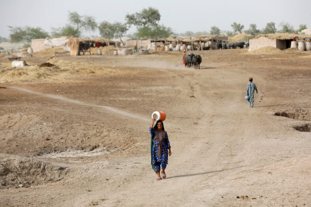 A woman walks to fetch water from a nearby hand-pump with a water cooler on her head, during a heatwave, on the outskirts of Jacobabad, Pakistan, on 16th May, 2022