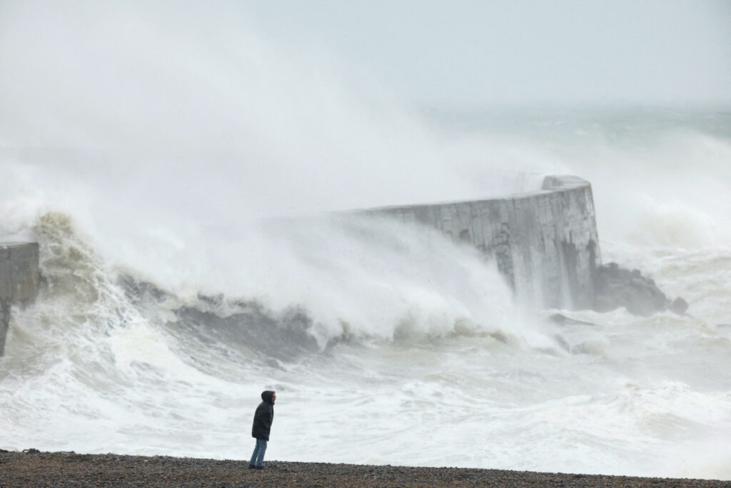 A person stands on the beach, while a wave crashes over Newhaven harbour wall, as Storm Ciaran hits the English coast, in Newhaven, Britain, on 2nd November, 2023