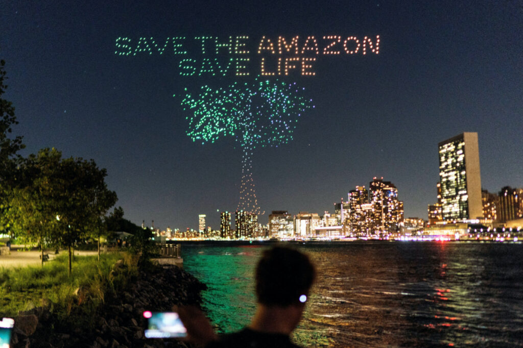 People watch drones creating a 3D display outside the United Nations Headquarters calling attention to the Amazon rainforest and climate change in New York US, on 15th September, 2023.