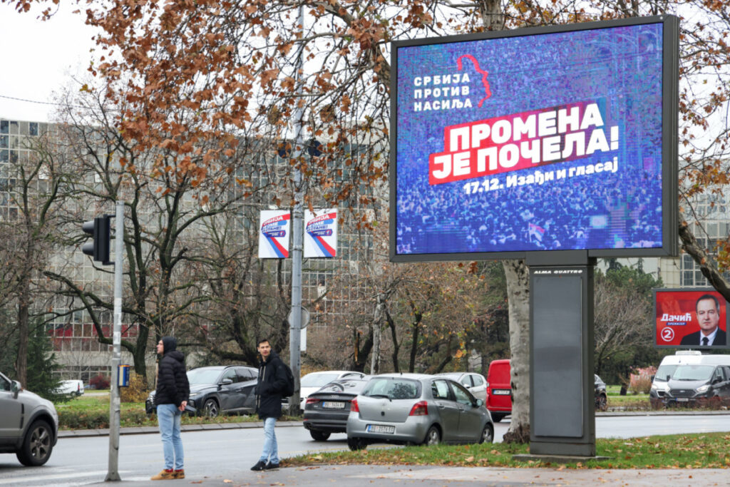People stand next to a pre-election billboard of the opposition coalition 'Serbia Against Violence' in Belgrade, Serbia, on 14th December, 2023.