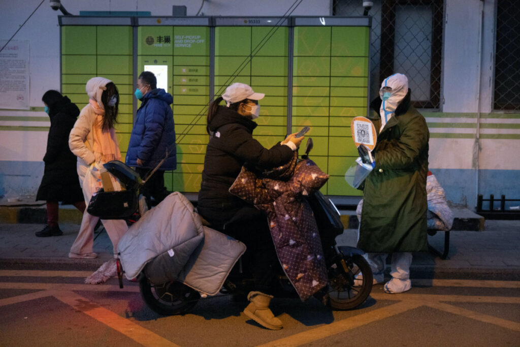 A woman presents her health code to a pandemic prevention worker in a protective suit to enter a residential compound as coronavirus disease outbreaks continue in Beijing, on 4th December, 2022
