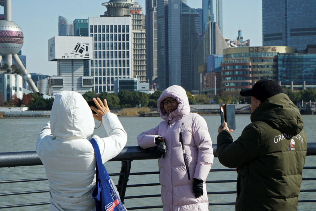 People wearing down jackets take pictures on the Bund on a cold winter day in Shanghai, China, on 21st December, 2023