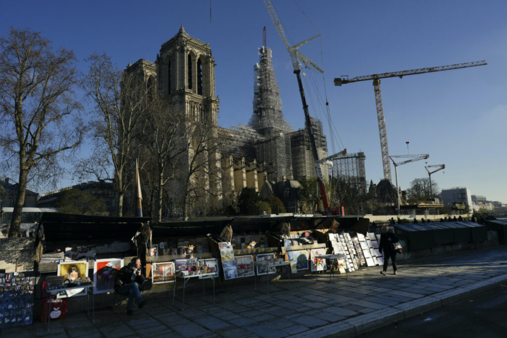 Book sellers wait in front of Notre-Dame de Paris cathedral, with its spire surrounded by scaffolding on Wednesday, 6th December, 2023 in Paris.