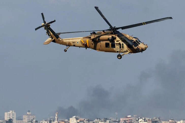 An Israeli military helicopter flies as smoke rises over Gaza, amid the ongoing conflict between Israel and the Palestinian Islamist group Hamas, as seen from southern Israel, on 6th December, 2023. 