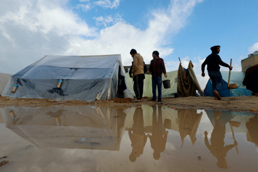 Displaced Palestinians, who fled their houses due to Israeli strikes, walk next to tents following heavy rains at tent camps, as the conflict between Israel and Hamas continues, in Rafah, in the southern Gaza Strip, on 13th December, 2023