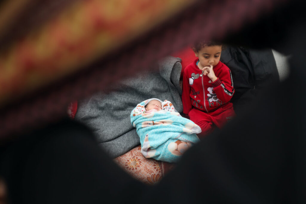 A girl sits next to Alma Al-Jadba, a twin Palestinian baby girl who was war born during the conflict between Israel and Hamas, in a tent where they shelter with their displaced family who fled their house due to Israeli strikes, in Rafah in the southern Gaza Strip on 17th December, 2023