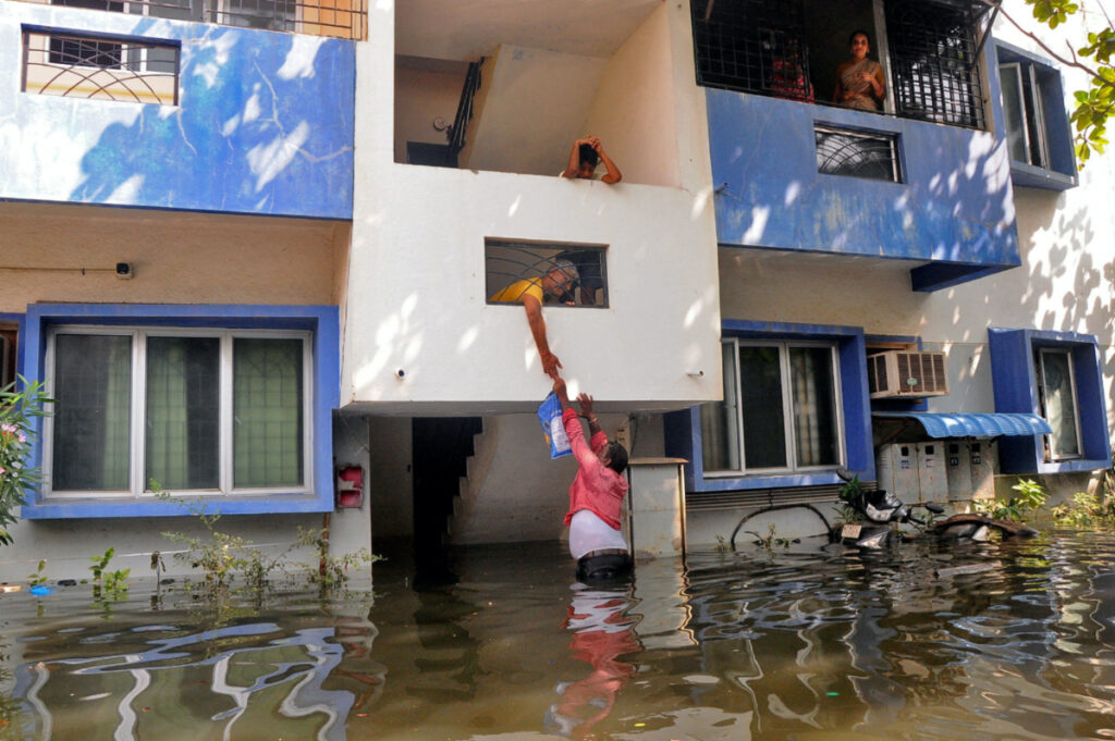 A volunteer offers food to a resident after his house got partially submerged following heavy rains due to Cyclone Michaung, in Chennai, India, on 6th December, 2023.