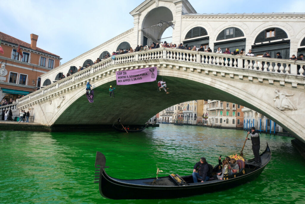 People ride in boats as waters of Grand Canal turned green after a protest by 'Extinction Rebellion' climate activists in Venice, Italy, on 9th December, 2023.