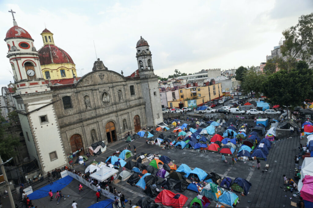 Migrants, mostly from Venezuela and Haiti, gather outside Our Lady of the Solitude church in a makeshift tent city camp as they wait for an appointment through the Customs and Border Protection app, called CBP ONE, in Mexico City, Mexico, on 28th November, 2023