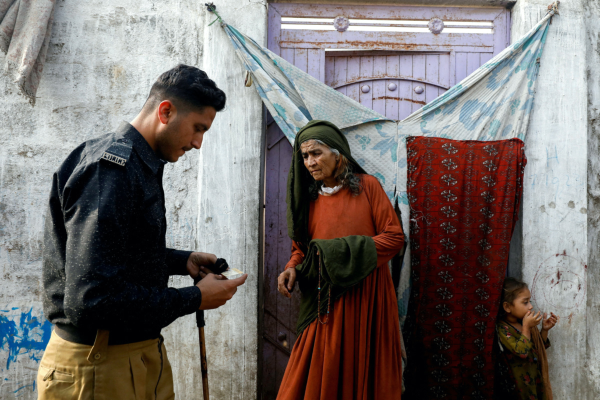 Edema Bibi, 66, an Afghan citizen, stands at the entrance of her house as a police officer checks her registration card, during a door-to-door search and verification drive for undocumented Afghan nationals, in an Afghan Camp on the outskirts of Karachi, Pakistan, on 21st November, 2023