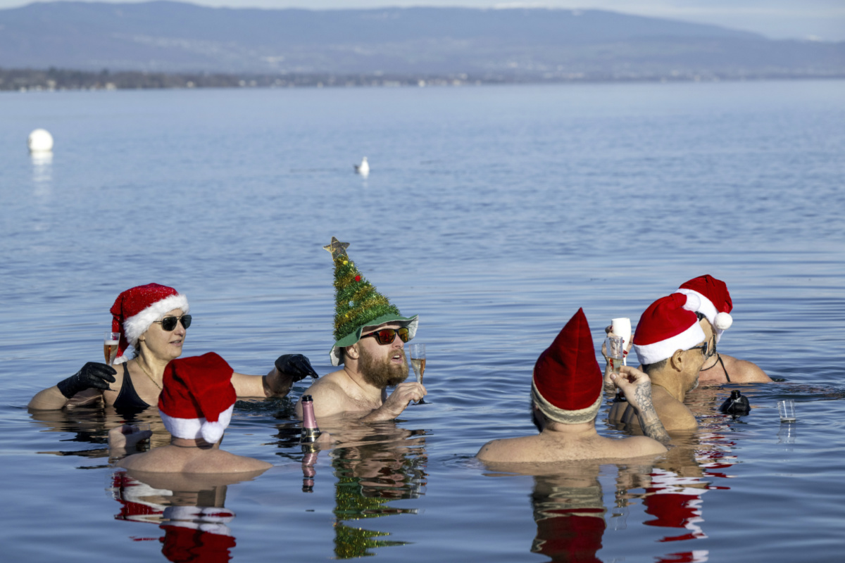 People drink as they swim with Santa hats in eight degree water in Lake Leman at Bains des Paquis on Christmas Eve, in Geneva, Switzerland, on Sunday, 24tH December, 2023