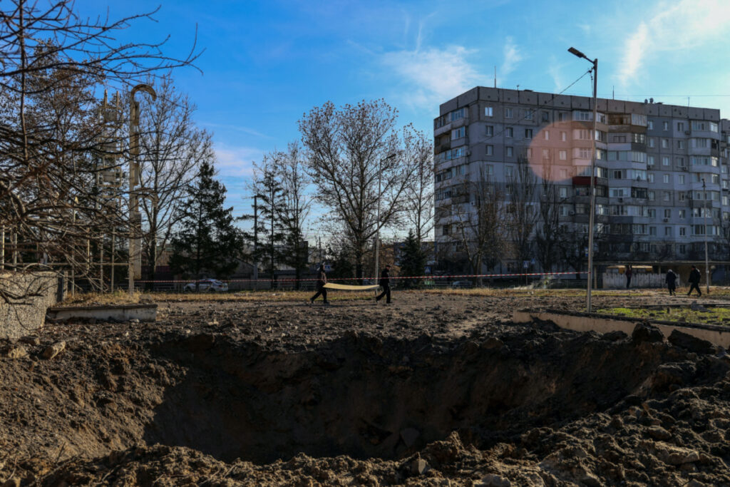 Local residents carry an OSB panel next to a crater from a Russian missile strike, amid Russia's attack on Ukraine, in Kherson, Ukraine on 5th December, 2023.