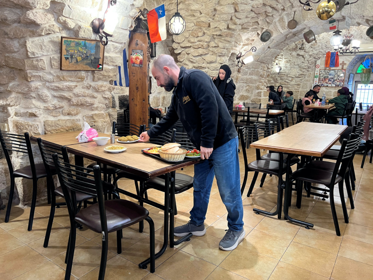 Fourth generation co-owner of Restaurant Afteem, Ala'a Salameh, 42, places food on a table inside the restaurant in Bethlehem, in the Israeli occupied West Bank, on 9th December, 2023.