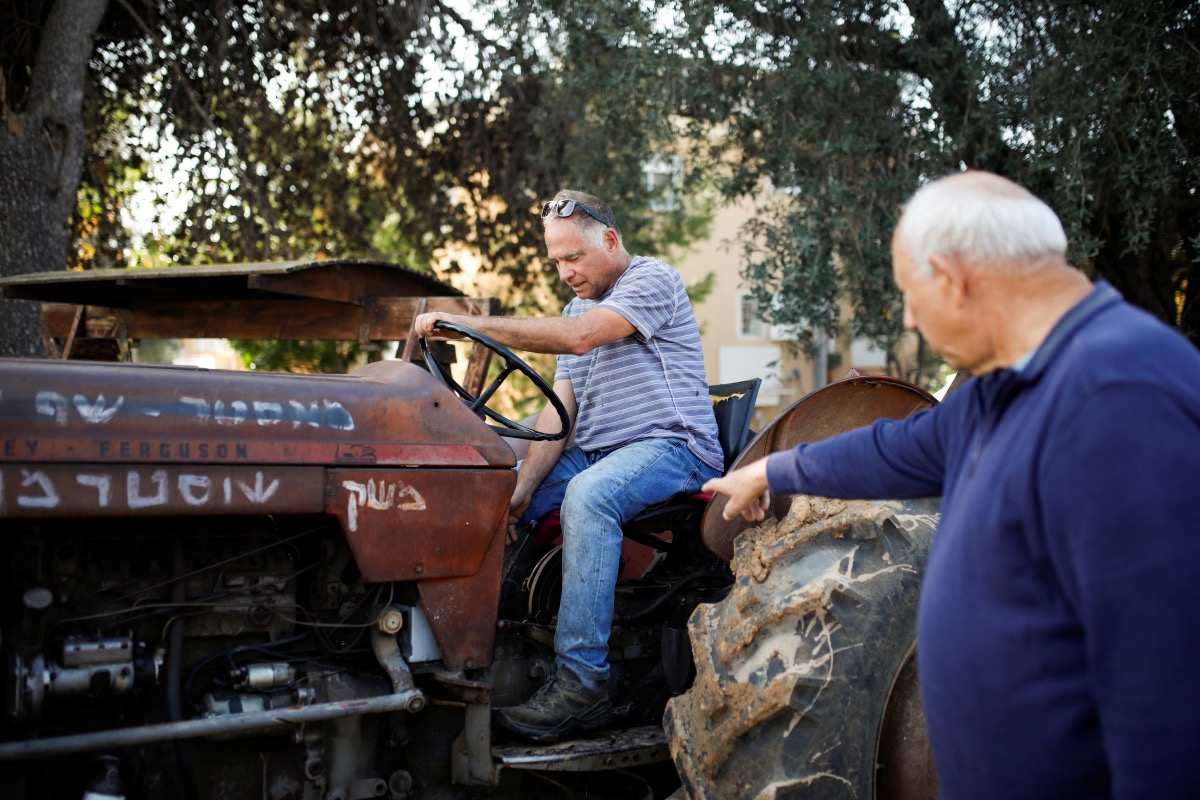 Yitzhak Shusterman points as a man uses a tractor at the Shusterman family farm where along with volunteers the family returns to work on the land despite having been evacuated due to the ongoing cross-border hostilities between Hezbollah and Israeli forces, in Liman, close to the Lebanese border in northern Israel, on 9th January, 2024.
