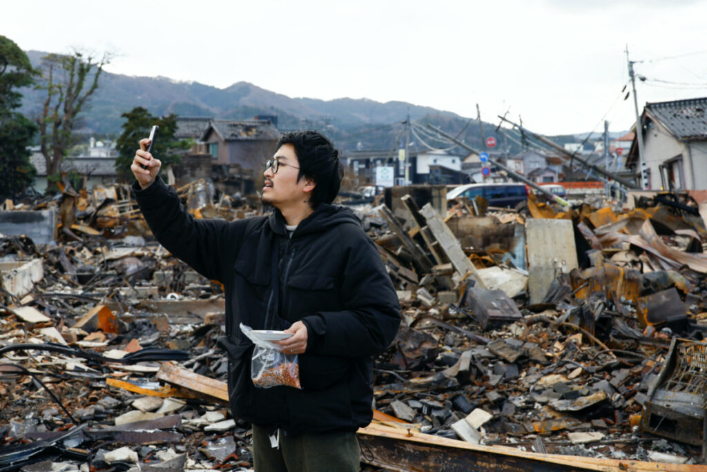 Japanese lacquer artist Kohei Kirimoto takes photos, while searching for his cats, next to an "Asaichi" morning market which burnt down in a quake-triggered fire, in Wajima, Japan, on 4th January, 2024