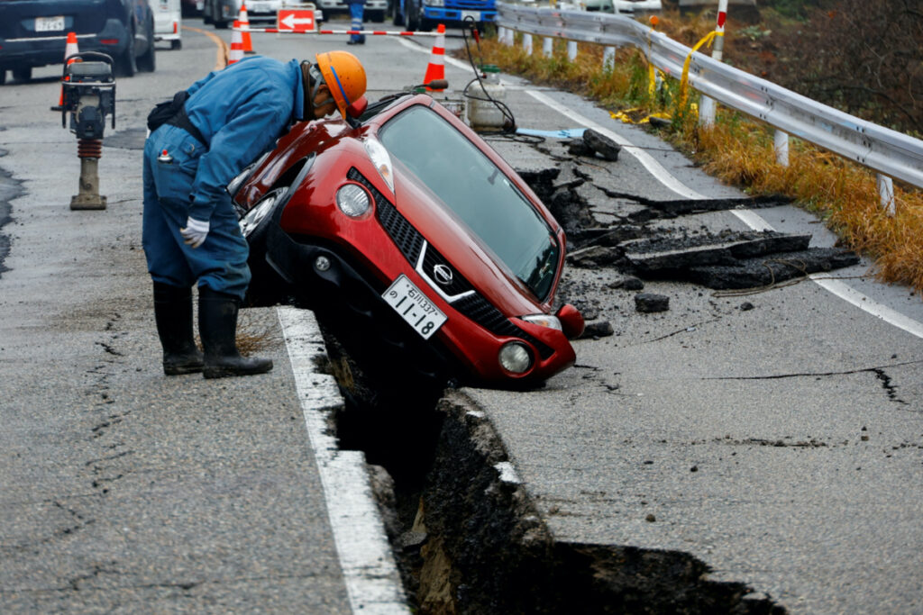 A worker looks at a car stuck on a broken road in the aftermath of an earthquake, near Anamizu, Japan, on 3rd January, 2024.
