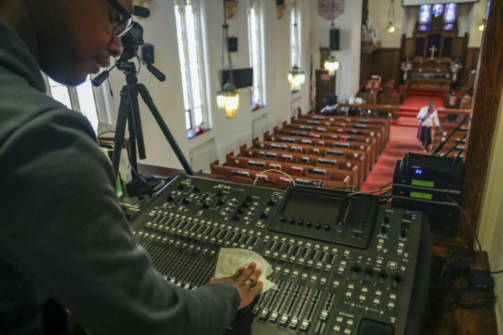 Multimedia technician Joseph Stoute, 21, use a disinfectant wipe to clean the audio equipment at St Paul's Methodist Church in Brooklyn, New York, where he directed a livestream online broadcast for home-bound congregants due to city-wide restrictions aimed at controlling the COVID-19 outbreak, on Sunday 22nd March, 2020, in New York